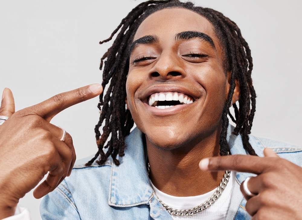 African American man with dreadlocks smiling and pointing at his teeth